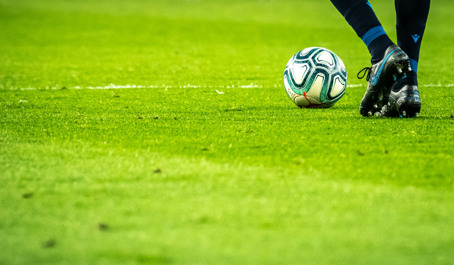 Çim sahada futbol topu ve oyuncunun kramponları; temsili futbol görseli
